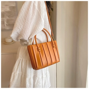 Detail view of orange bucket bag with pleated leather texture and gold hardware