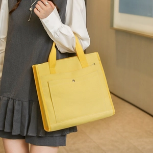 Close-up of bright yellow canvas tote bag featuring front pocket and metallic button detail