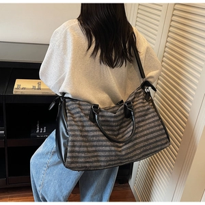 Detail of grey striped travel bag with black leather straps and large capacity design