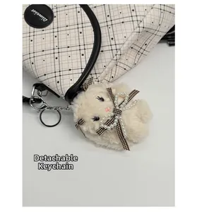 Detail of detachable cream plush bear charm with pearl bow on black and white plaid bag