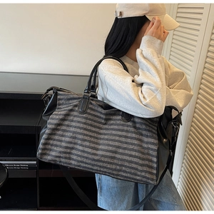Detail of grey striped travel duffel bag with black leather handles and shoulder strap