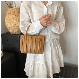 Brown pleated bucket bag with cylindrical handle shown in a stylish lifestyle scene