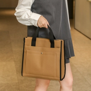 Detail of khaki canvas tote bag featuring black webbing handles and a metal snap pocket
