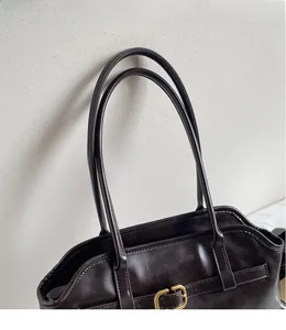 Détail des coutures des anses en cuir marron foncé et de la boucle dorée du sac cabas