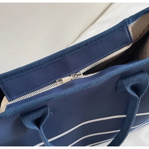 Detail view of navy canvas tote bag featuring silver metal zipper and white striped pattern