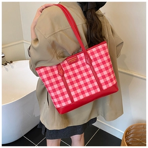 Detail of red gingham tote bag featuring leather handles and stitched logo patch