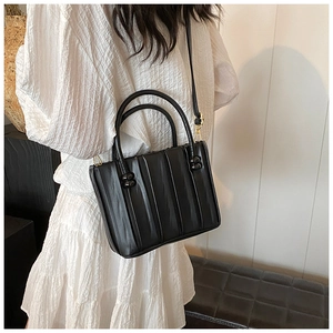 Model wearing black pleated leather tote bag with gold hardware and side ball ornament