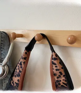 Detail of wide leopard print shoulder strap featuring black leather trim on a wooden hook