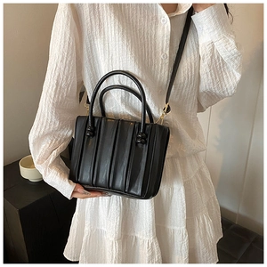 Detail of black pleated tote bag with vertical textures and matching shoulder strap