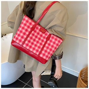 Detail of red and pink checkered tote bag featuring a leather logo patch and long straps