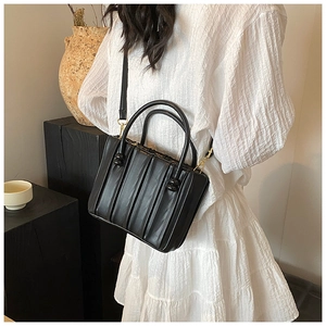 Detail of pleated black crossbody tote bag with gold hardware on a model outfit