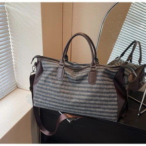 Detail of striped travel bag with brown leather trim and metal hardware on a counter
