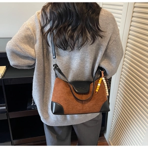 Detail of brown suede crossbody bag with black leather flap and beaded charm accessory