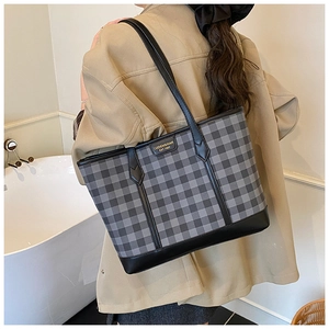 Detail of gray checkered tote bag with reinforced black leather straps on female model