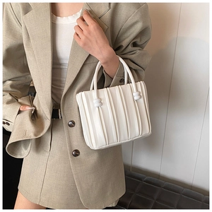 Detail of white leather bucket bag featuring vertical pleated texture and cylindrical accents