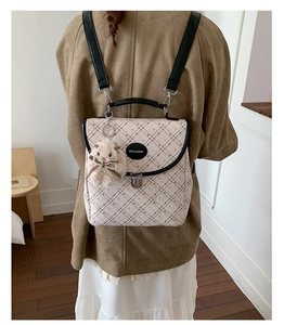 Detail of checkered backpack with rabbit plush charm and metallic clasp closure
