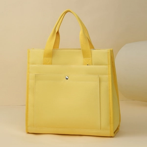 Detail of yellow canvas tote bag featuring front pocket and silver metal button fastener
