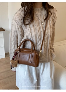 Dettaglio di una borsa Boston marrone con ciondolo a orsetto e logo in rilievo su pelle