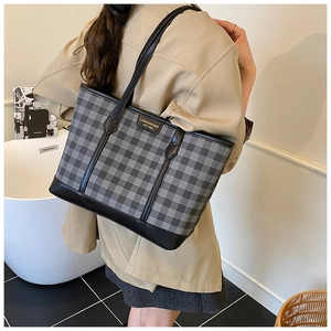 Close-up of checkered tote bag featuring a gold logo plate and premium leather stitching