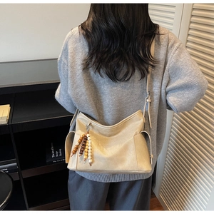 Detailed side view of beige bucket bag with beaded tassel and soft pebbled leather texture