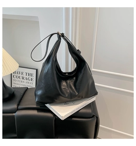 Detail shot of a minimalist black faux leather hobo bag on a chic woven stool