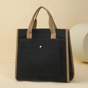 Detailed close-up of a black canvas tote bag with khaki contrast handles and metal button pocket