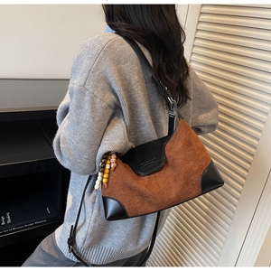 Detail of a brown suede crossbody bag featuring a black leather base and decorative wooden beads