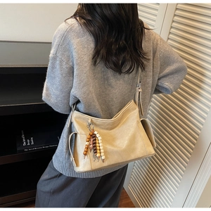 Detail of beige faux leather crossbody bag with wooden bead charm and cargo side pocket