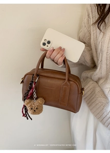 Dettaglio della borsa vintage in pelle marrone con scritte a rilievo e ciondolo a orsetto