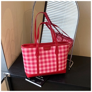 Detail of red and pink checkered tote bag featuring leather straps and metal brand plate