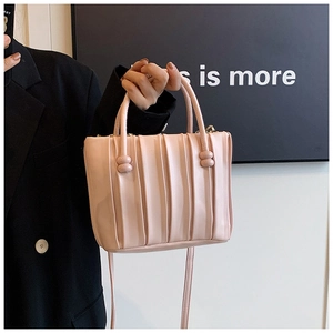 Detail of light pink pleated handbag featuring spherical decorative buckles and slim strap