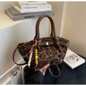 Detail of leopard print crossbody bag with wooden bead charm and leather handles
