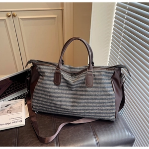 Detail view of striped travel bag with brown leather handles and a removable shoulder strap