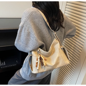 Detail of hobo crossbody bag in beige soft leather with decorative wooden bead charm
