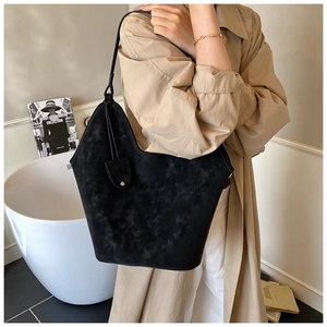 Close-up of black suede tote bag styled with a trench coat in a minimal interior