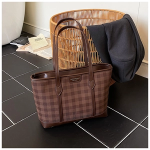 Close-up of brown checkerboard tote bag with golden brand plaque on a stylish background