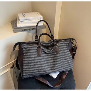 Detail view of large striped canvas travel bag with brown leather straps and metal zippers