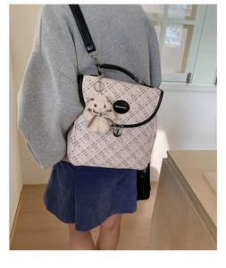 Detail of a cream plaid backpack with black trim and a cute plush bunny charm accessory