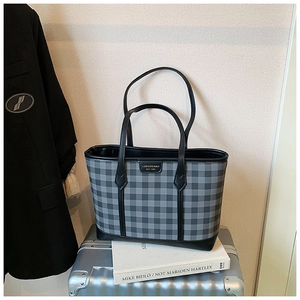 Detailed close-up of a plaid tote bag with leather handles on a silver suitcase for travel