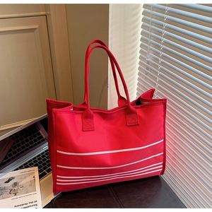 Detail of red canvas tote bag with white stripes on a desk with a laptop