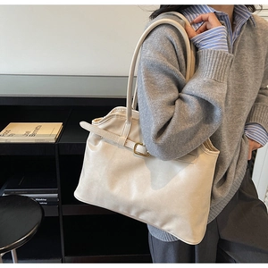 Détail d'un sac cabas en cuir crème avec des plis latéraux et des sangles à boucles