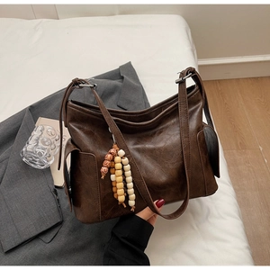 Detail of retro brown tote bag with beaded charm and side pocket on neutral background