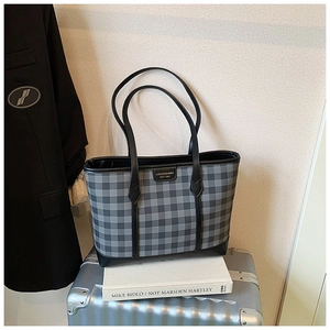 Detail of plaid tote bag with leather straps and metal logo on a travel background