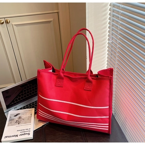 Detailed close-up of large red canvas tote bag with white stripes on a brown desk