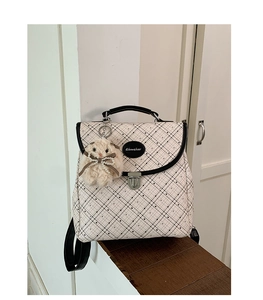 Detail of plaid backpack featuring metal buckle and plush rabbit charm with pearl bow
