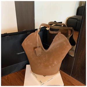Detail of a brown suede tote bag featuring a V-shaped opening and a leather charm