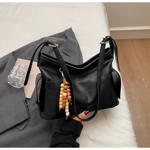 Detail of black large-capacity hobo bag featuring side pocket and wood bead tassel