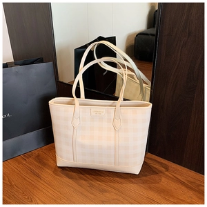 Detail of cream plaid tote bag featuring metal brand logo and premium stitched leather handles