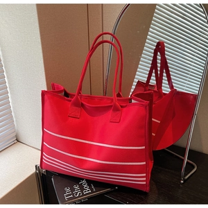 Detail of red canvas tote bag with white stripes and long handles on a mirror surface