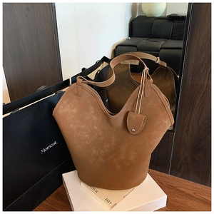 Close-up of brown suede tote bag with V-shaped top and shield charm on magazines